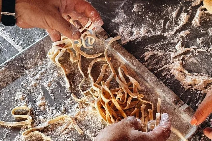 Hände heben frische Pasta von einem bemehlten Brett