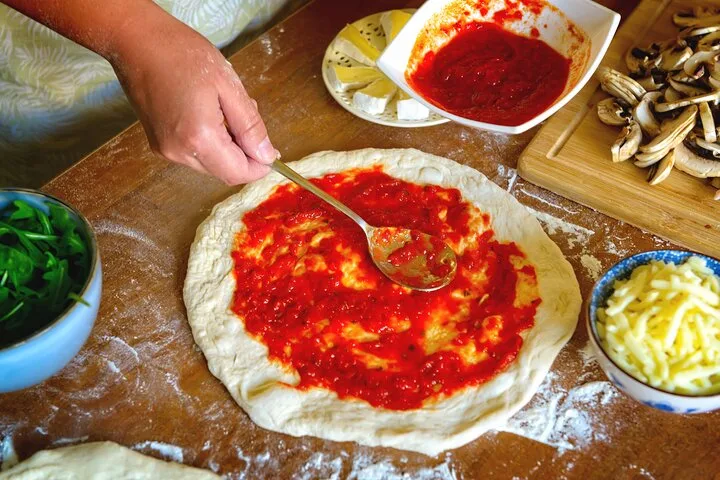 Tomatensauce wird auf einem Pizzaboden verteilt